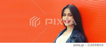 Portrait of beautiful brunette smiling young woman model posing in black leather jacket on red 115039010