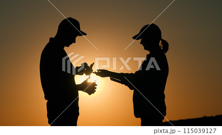 A couple of farmers are standing in a field at sunset, examining a plant and using a tablet. A couple of farmers are standing in a field at sunset, examining a plant and using a tablet. 115039127