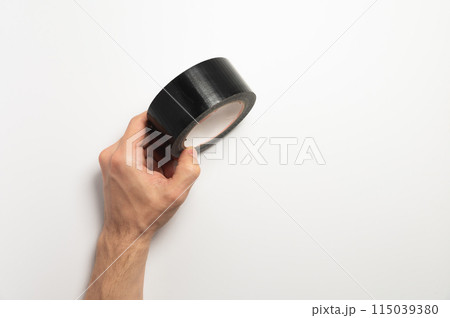A roll of black reinforced adhesive tape, for sealing joints of roofing materials, when installing the roof, lying, on a white background in a man hand 115039380