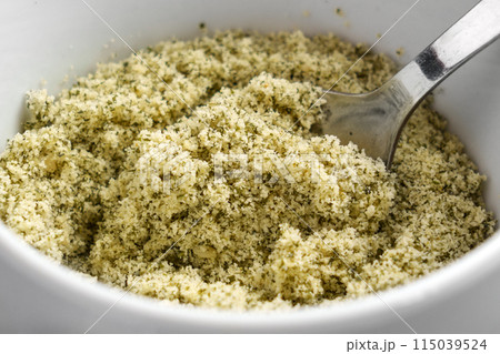 Ground crushed pumpkin seeds as a raw ingredient for dietary pastry in white kitchen cup with spoon Ground crushed pumpkin seeds as a raw ingredient for dietary pastry in white kitchen cup with spoon 115039524