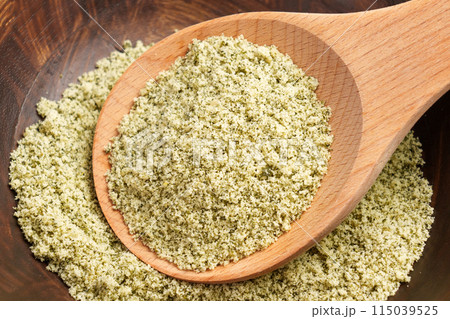 Green ground crushed pumpkin seed flour as a raw ingredient for dietary pastry in brown wooden bowl with rustic spoon. Close up Green ground crushed pumpkin seed flour as a raw ingredient for dietary pastry in brown wooden bowl with rustic spoon. Close up 115039525