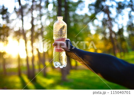 A woman's hand holds a bottle of water against a spring forest background. 115040701