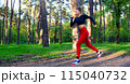 A young woman is running through the park in a tracksuit. 115040732