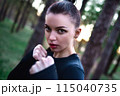 Portrait of a woman in a fighting pose doing martial arts training for a fist bump against a forest background. 115040735