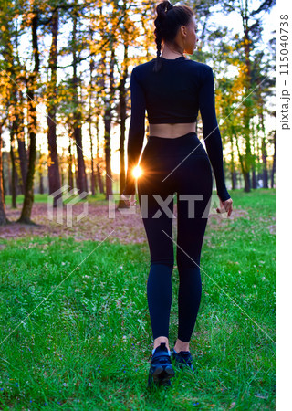 Shapely woman in black tight suit walking in nature in the woods in the sunlight. Shapely woman in black tight suit walking in nature in the woods in the sunlight. 115040738