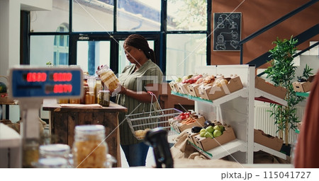 African american client opening jars filled with bulk items to buy chemicals free products and supplies. Woman searching for eco friendly vegan food alternatives, nonpolluting concept. Handheld shot. African american client opening jars filled with bulk items to buy chemicals free products and supplies. Woman searching for eco friendly vegan food alternatives, nonpolluting concept. Handheld shot. 115041727