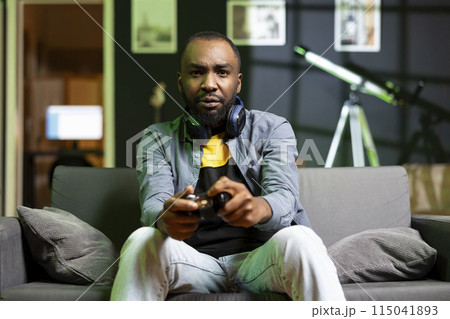 Gamer showing concern after being outsmarted by enemies while playing videogames on console. African american man feeling annoyed after being defeated while playing games with gamepad 115041893