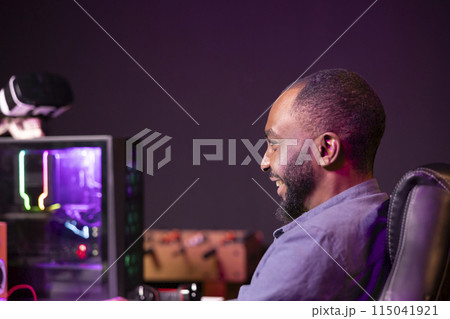 Gamer laughing at home, having fun playing videogames on computer. Joyous african american man contending in gaming tournament using powerful neon lit desktop PC in apartment 115041921
