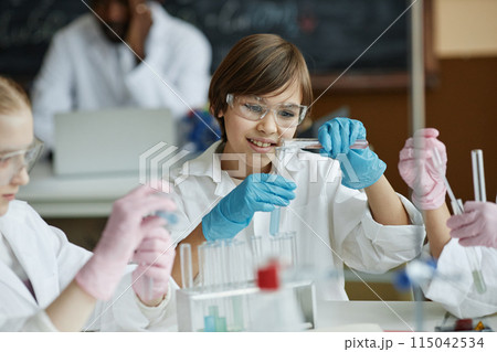 Curious Caucasian boy sitting at table in classroom mixing liquids in test tube during lab experiment in Chemistry class 115042534