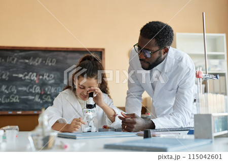 Young African American teacher of Chemistry wearing lab coat giving microscope slide to Middle Eastern student, copy space Young African American teacher of Chemistry wearing lab coat giving microscope slide to Middle Eastern student, copy space 115042601