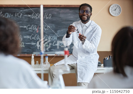 Over-the-shoulder shot of cheerful young African American teacher of Chemistry wearing white lab coat conducting lesson 115042750