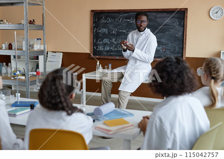 Young African American teacher of Chemistry speaking about molecular structure during lesson at school 115042757