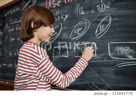 Medium shot of Caucasian schoolboy wearing casual clothes writing on blackboard in English class, copy space Medium shot of Caucasian schoolboy wearing casual clothes writing on blackboard in English class, copy space 115042779