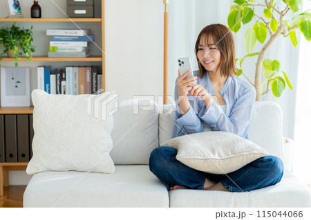 リビングでスマホを見る若い女性 115044066