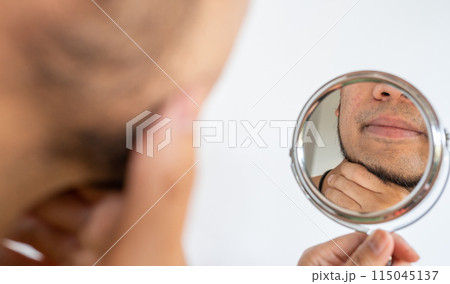 Cropped shot of Asian man touching his beard grows on a part of his lower face while looking his face by mirror. Beard can make you feel more attractive. 115045137