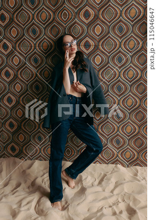 Woman in an unbuttoned jacket and jeans posing against a wall Woman in an unbuttoned jacket and jeans posing against a wall 115046647