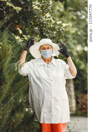 Old woman in a medical mask. Portrait of beautiful aged woman in the park. Grandma in a white hat. Old woman in a medical mask. Portrait of beautiful aged woman in the park. Grandma in a white hat. 115047770