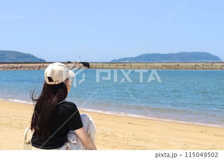 海辺 砂浜 女性 砂浜にいるロングヘアの女性 砂浜に座り海を眺めている様子 海辺 砂浜 女性 砂浜にいるロングヘアの女性 砂浜に座り海を眺めている様子 115049502