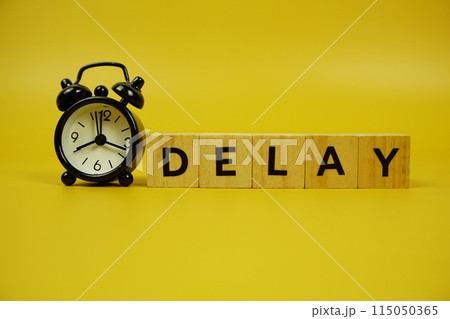 Delay with wooden blocks alphabet letters and alarm clock on yellow background 115050365