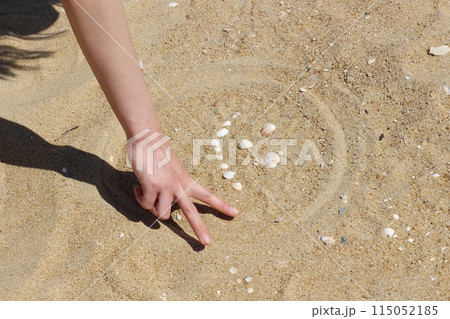 砂浜で貝殻を並べて作った顔の輪郭を指で書く女性の手 ピースをする手 砂浜で貝殻を並べて作った顔の輪郭を指で書く女性の手 ピースをする手 115052185