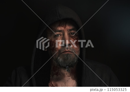 Closeup portrait of an injured man. Scary man in a hood with a bloody face Closeup portrait of an injured man. Scary man in a hood with a bloody face 115053325