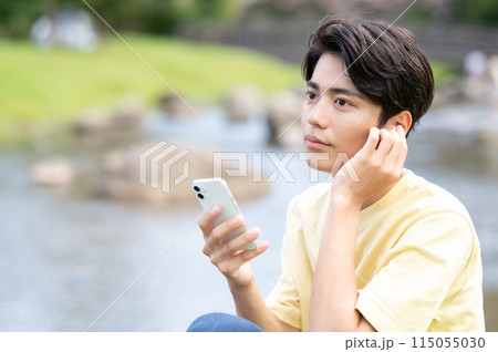 水辺で音楽を聴く若い男性 115055030
