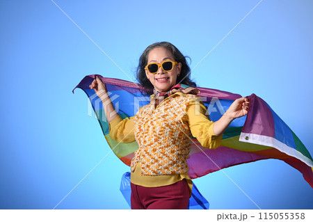 Older lady holding a rainbow flag on blue background LGBT, human rights, freedom and equality concept 115055358