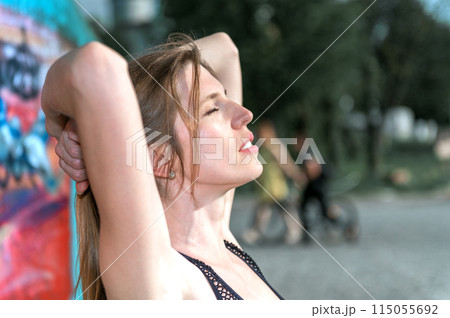 Young woman resting after doing gymnastics on the street. Portrait of fit and sporty young woman doing stretching in city. 115055692
