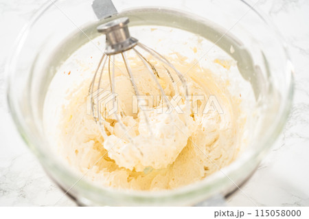 Mixing ingredients in a large glass mixing bowl of kitchen mixer to make eggnog buttercream frosting. 115058000