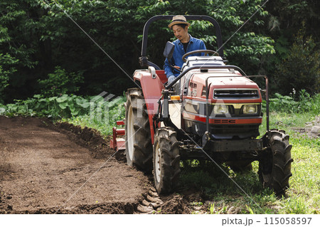 トラクターで畑を耕す若い男性 115058597