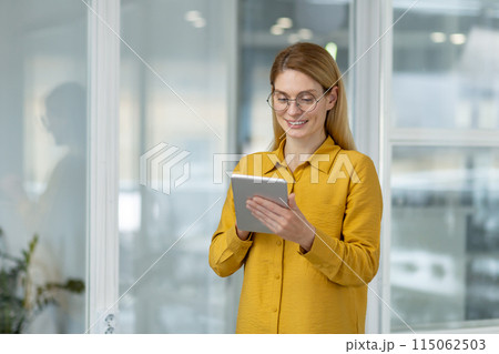 Smiling woman using a tablet in a bright, modern office environment. Ideal for business, technology, and workplace concepts. Smiling woman using a tablet in a bright, modern office environment. Ideal for business, technology, and workplace concepts. 115062503