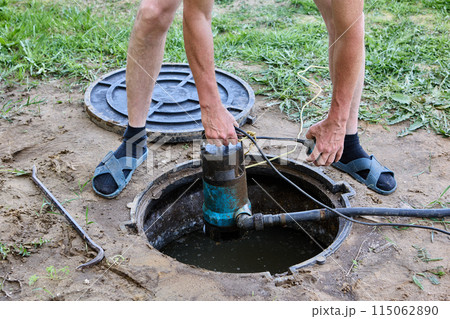 Worker plunges sewage pump into waste water of septic tank to pumping out wastewater before servicing tank. Worker plunges sewage pump into waste water of septic tank to pumping out wastewater before servicing tank. 115062890