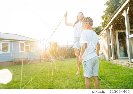 Joyful kid with mother playing with water sprinkler hose, splashing, laughing, having fun together in garden on sunset. Summer outdoor activity. Happy active childhood, family time. Selective focus. Joyful kid with mother playing with water sprinkler hose, splashing, laughing, having fun together in garden on sunset. Summer outdoor activity. Happy active childhood, family time. Selective focus. 115064466
