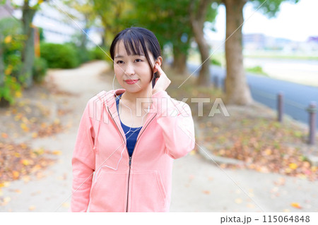 有線イヤホンで音楽を聴きながらウォーキングする若い女性　ボディメイク　ランニングウェア　 115064848