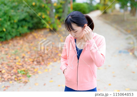 有線イヤホンで音楽を聴きながらウォーキングする若い女性　ボディメイク　ランニングウェア　 115064853