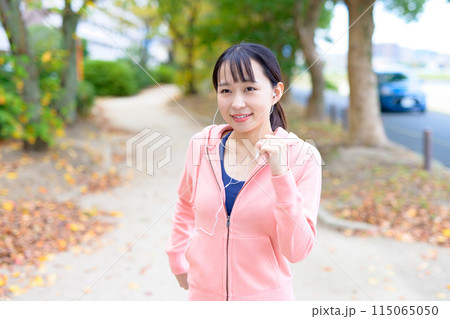 有線イヤホンで音楽を聴きながらウォーキングする若い女性　ボディメイク　ランニングウェア　 115065050