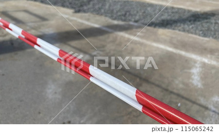 Red and white striped tape to indicate road work against the background of road being repaired, fencing danger zone at construction site Red and white striped tape to indicate road work against the background of road being repaired, fencing danger zone at construction site 115065242