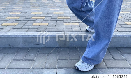 Girl comes down the stairs in blue wide jeans and white sneakers in city street 115065251