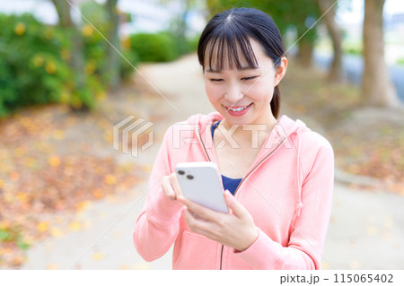 スマホを見ながらウォーキングする若い女性　ボディメイク　ランニングウェア　 115065402