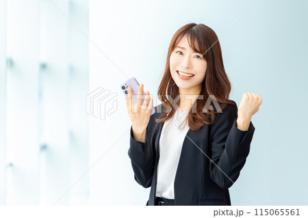 スマートフォンを持ってガッツポーズをする笑顔のビジネスウーマン 115065561