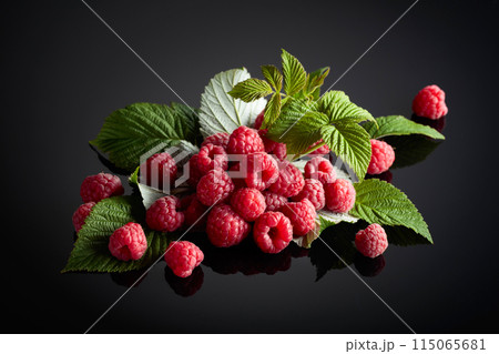 Fresh raspberries with leaves on a black background. Fresh raspberries with leaves on a black background. 115065681