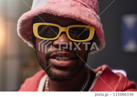 Extreme closeup portrait of Black man wearing retro sunglasses and fuzzy hat looking at camera in motion 115066336