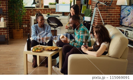 Multiethnic mates invited to birthday party offering presents to cheerful African american man impressed by nice gesture. Guests surprising their friend with thoughtful present and enjoying appetizers Multiethnic mates invited to birthday party offering presents to cheerful African american man impressed by nice gesture. Guests surprising their friend with thoughtful present and enjoying appetizers 115069091