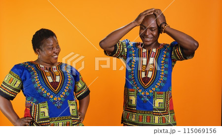 Joyful man and woman laughing together in studio, having fun with silly jokes over orange background. African american people enjoying funny moments with laugh, amused couple. 115069156