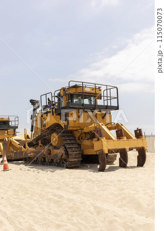 Yellow Crawler Dozer On Sandy Beach, Blue Sky On Background. Bulldozer Builds Roads. Construction And Landfill Equipment And Machinery. No People. Vertical Plane Yellow Crawler Dozer On Sandy Beach, Blue Sky On Background. Bulldozer Builds Roads. Construction And Landfill Equipment And Machinery. No People. Vertical Plane 115070073