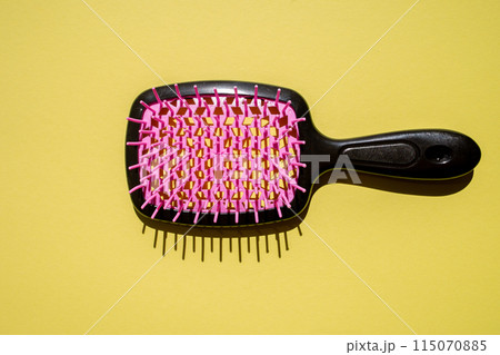 Top view of a black hair brush on a vibrant yellow surface, 115070885