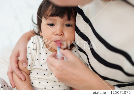 mother feeding liquid medicine to baby girl by syringe. sick toddler mother feeding liquid medicine to baby girl by syringe. sick toddler 115071076