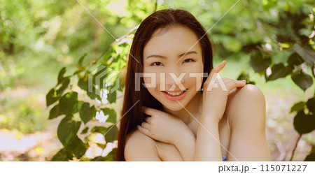 Close up outdoor portrait Beautiful young Chinese Asian woman perfect skin posing outside sunny summer day green foliage. Natural facial treatment. Cosmetology, skin care and spa. Fragnance concept. 115071227