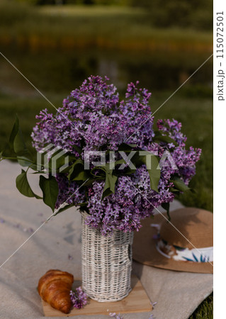 Bouquet of lilacs in a wicker vase, croissant and hat. Spring Picnic 115072501