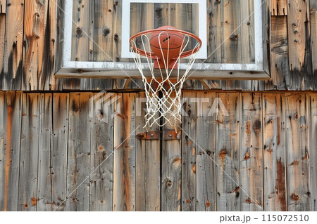 A rustic, old-school basketball hoop attached to a barn, with a classic leather basketball 115072510